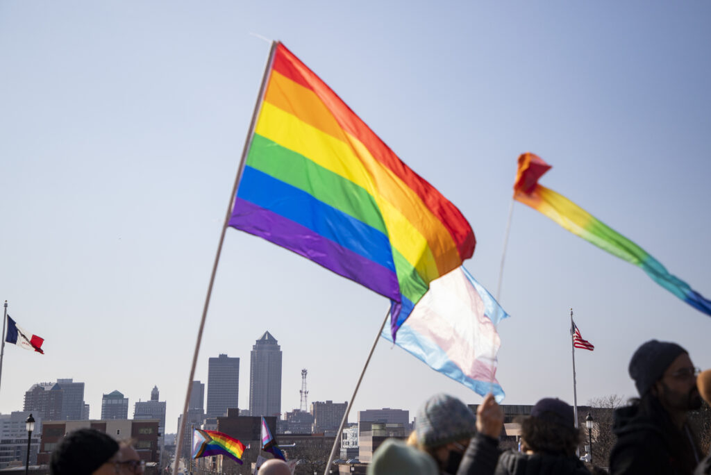 Rainbow LGBTQ pride flags fly in the foreground of the Des Moines skyline.