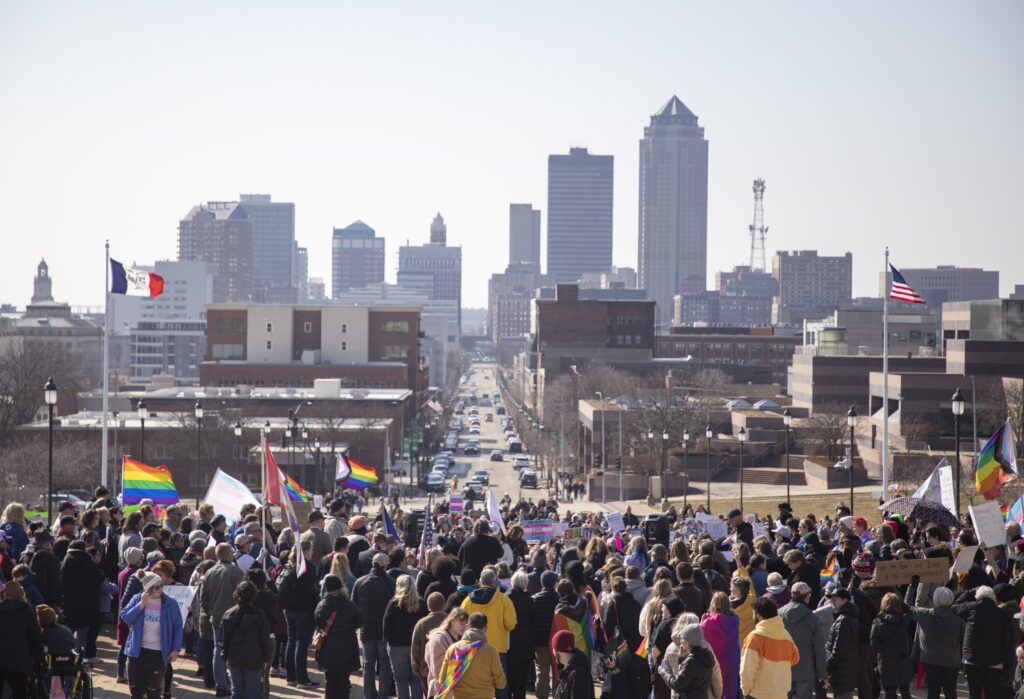 A large crowd gathers in front of the Des Moines skyline.