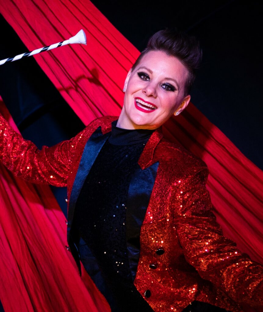 A photo of Felicia Coe, who is wearing a red ringmaster coat and is holding a baton.