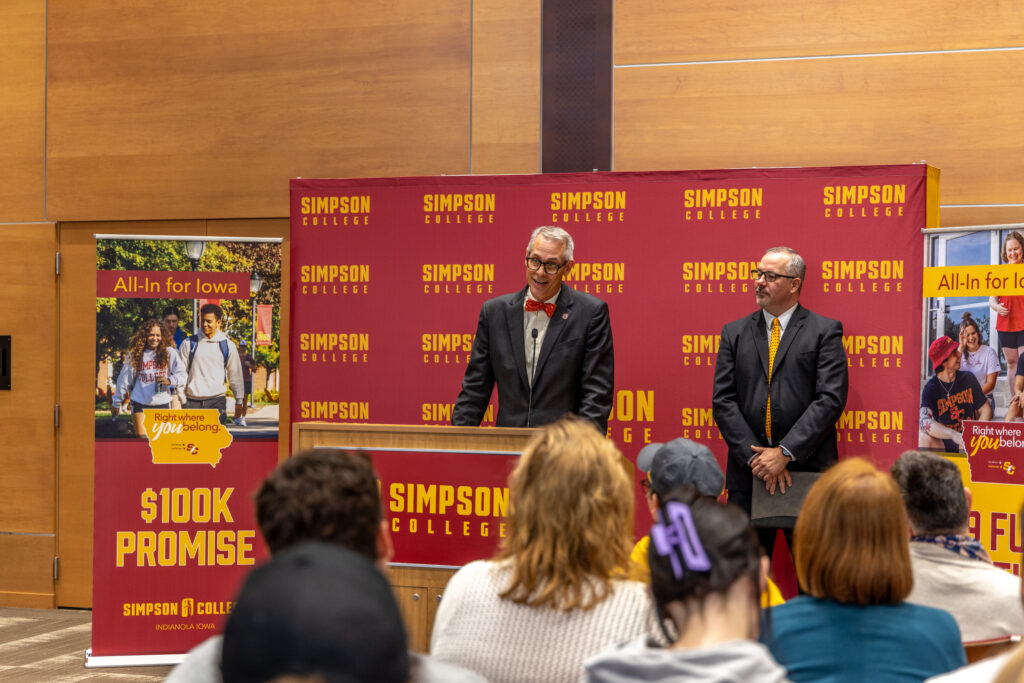 Jay Byers stands at a podium with a Simpson College background behind him.
