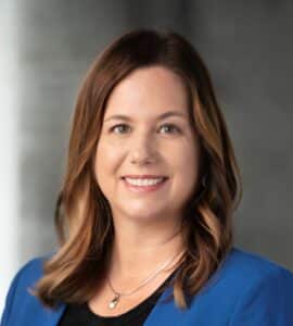 A white woman with brown hair wearing a blue jacket and black shirt