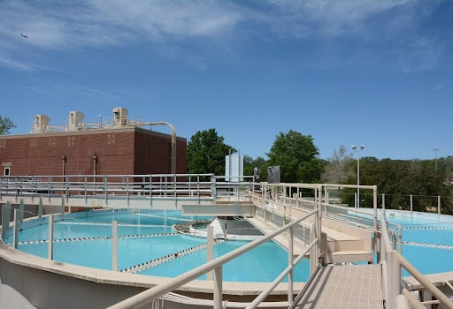 A water treatment plant showing a pool of water with walkways and a brick building behind it.