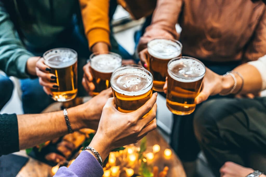 Group of friends drinking and toasting glass of beer at brewery pub restaurant Happy multiracial people enjoying happy hour with pint sitting at bar table Youth Food and beverage lifestyle concept