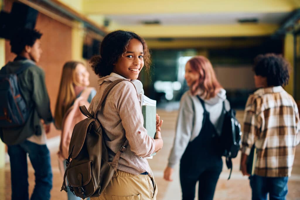 Happy black teenage girl in high school hallway looking at camera.
